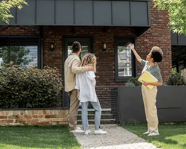 a realtor talks to clients outside a brick home