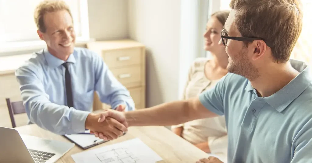 A couple sitting at a table with a landlord, signing a rental agreement.