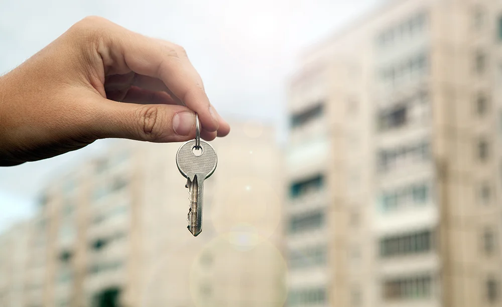 A hand holding keys with an apartment complex in the background.