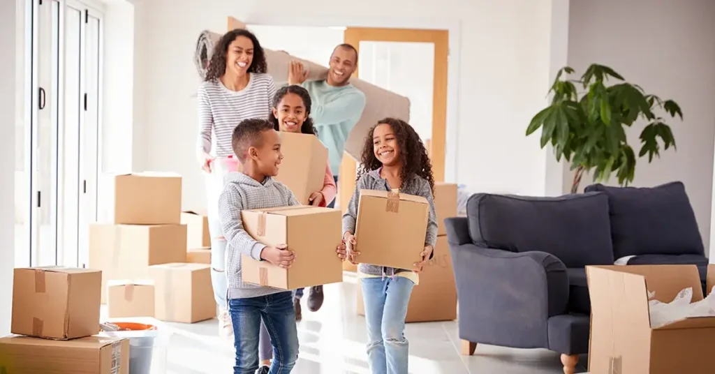 A family with three young children smiling and moving into their new home.