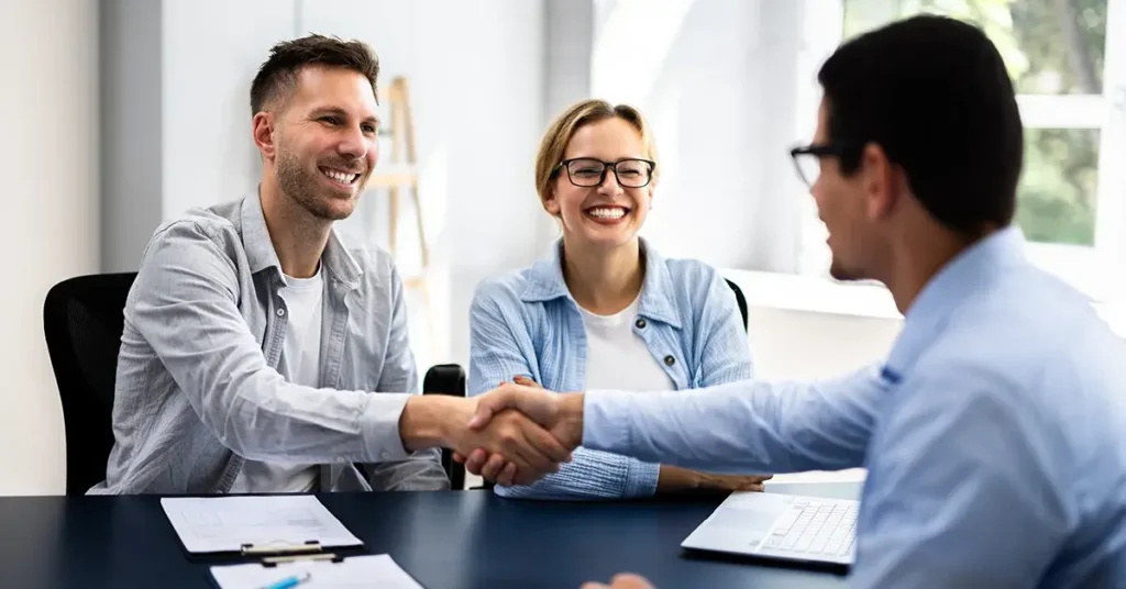 A couple shaking hands with their landlord and smiling.