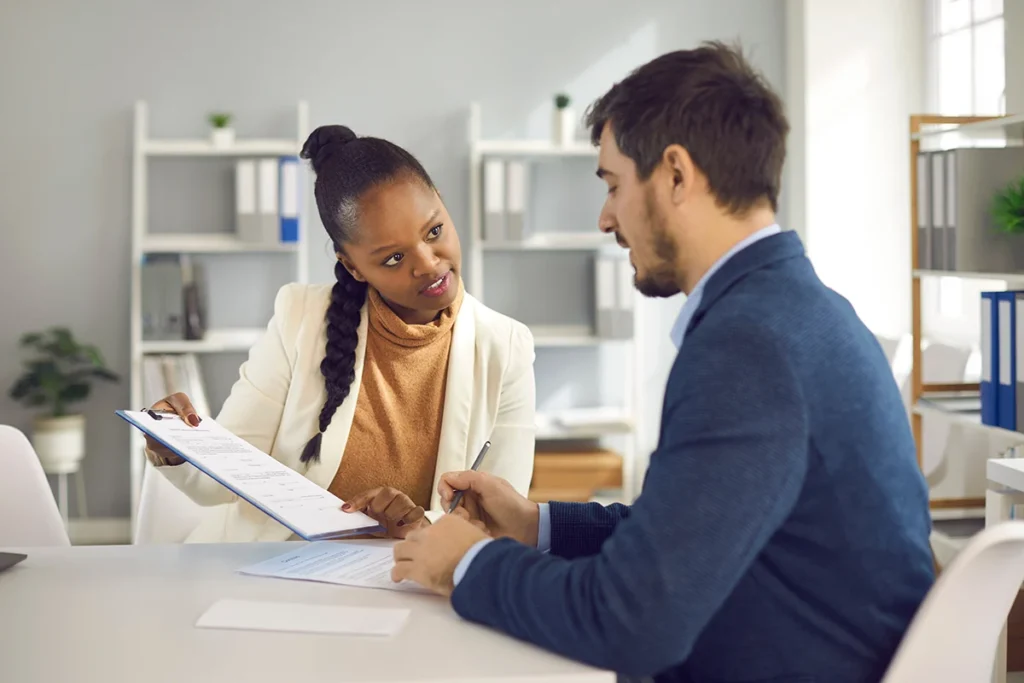female solicitor pointing at insurance contract showing male client where to write signature.