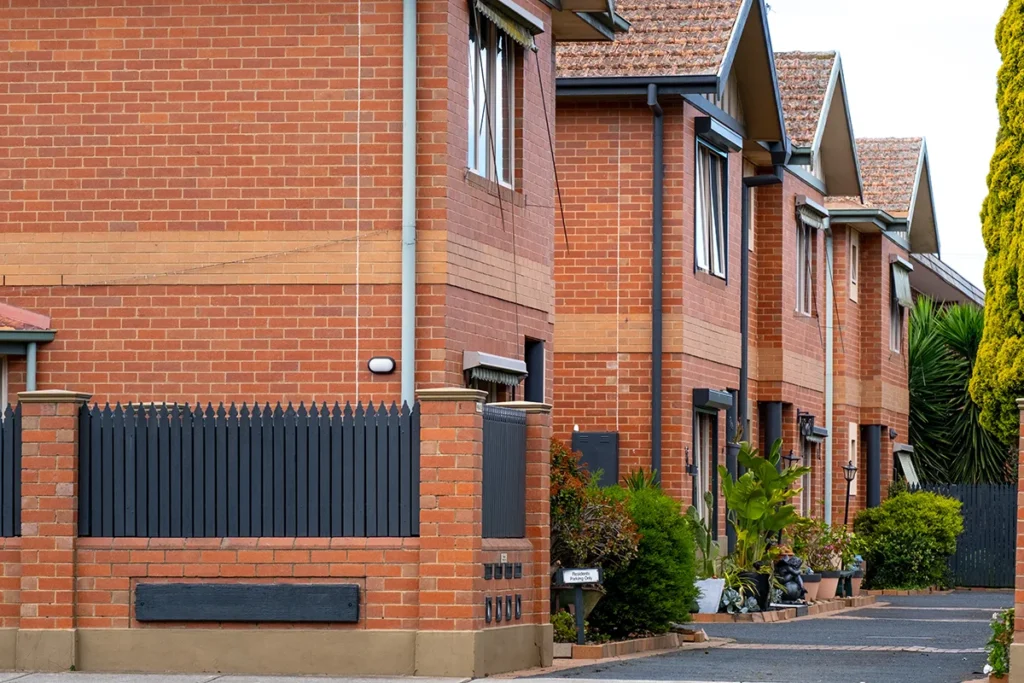 A row of older brick townhouses with repetitive architectural design and uniform terracotta roofing in a suburban residential neighborhood