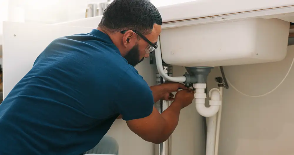 A plumber repairing pipes under a sink.