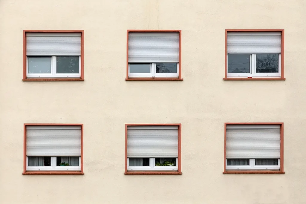 Exterior view of windows on a tan wall. Windows have the shades drawn to different levels.