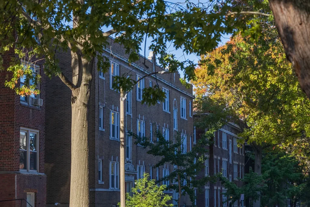 Exterior shot of an older, brick apartment building with trees in the foreground.