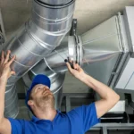 St. Louis rental property HVAC maintenance being performed by a man in a blue hat stnading under ductwork.
